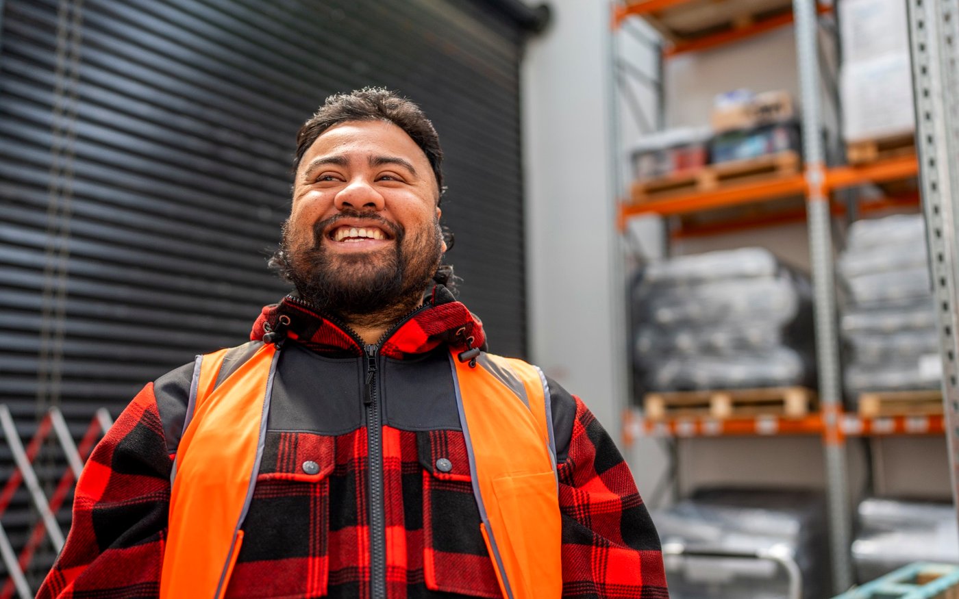 A smiling warehouse worker in hi-vis and a red check jacket