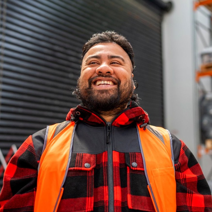 A smiling tradie in a red bush shirt and hi-vis vest