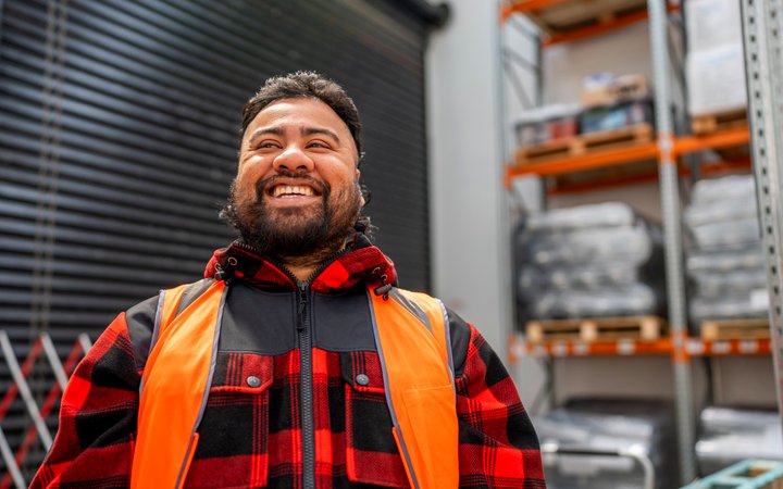 A smiling warehouse worker in hi-vis and a red check jacket